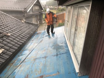 青く塗られた古いトタン屋根を洗っているいる様子