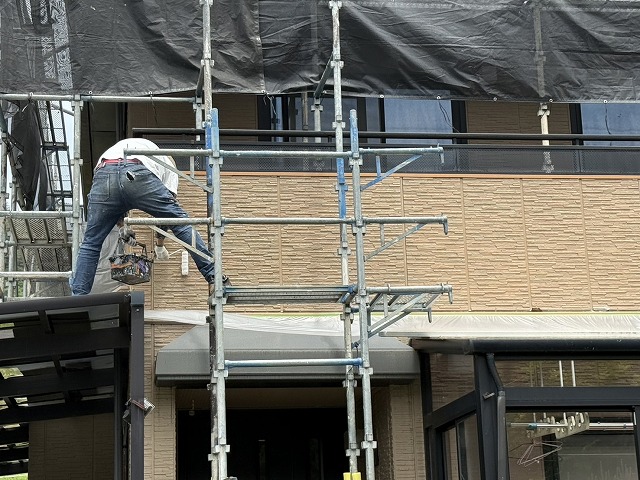 足場の上で外壁塗装の下塗りを行う塗装職人の様子