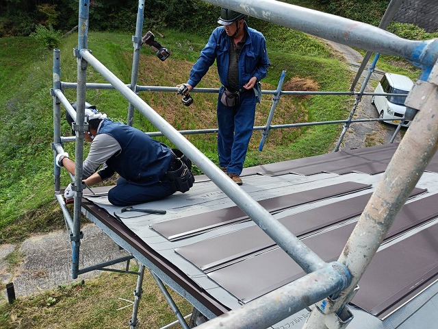 倉庫建物の軒先でSGL鋼板を張り始める作業員の様子