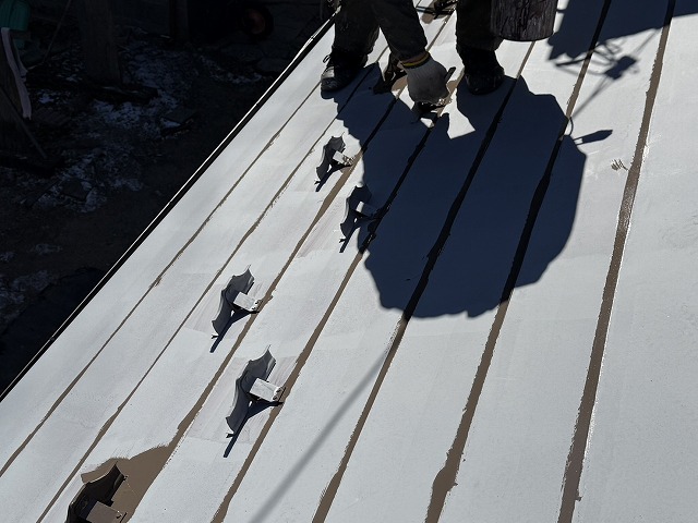 屋根材の重なり部分や雪止め金具周囲にハケで先行塗りを行っている中塗り施工