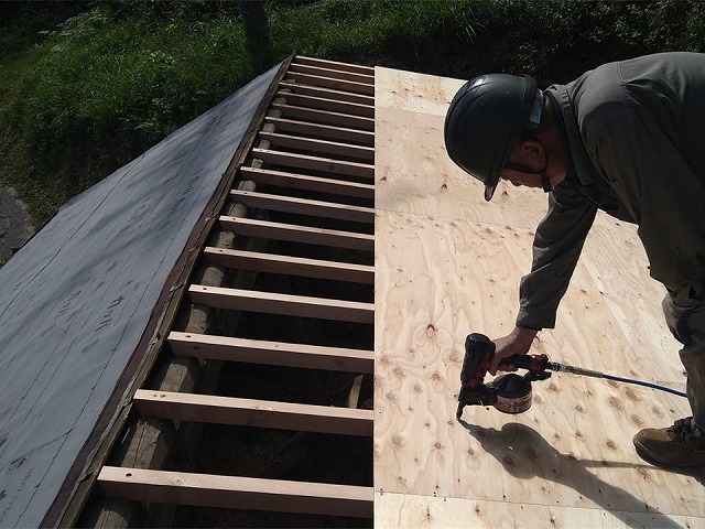 垂木の上に構造用合板の野地板を釘打ちで固定する作業員の様子
